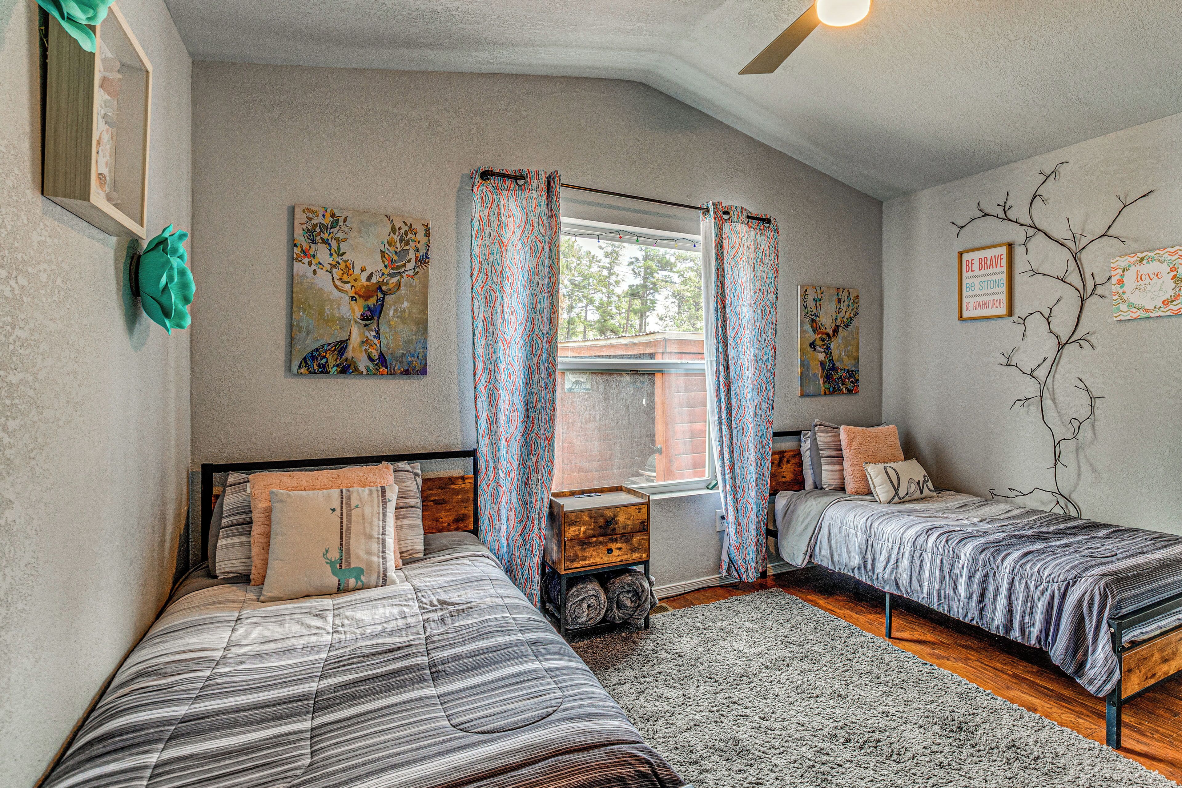 A bedroom with two beds, a window with curtains, a radiator, and wall art.