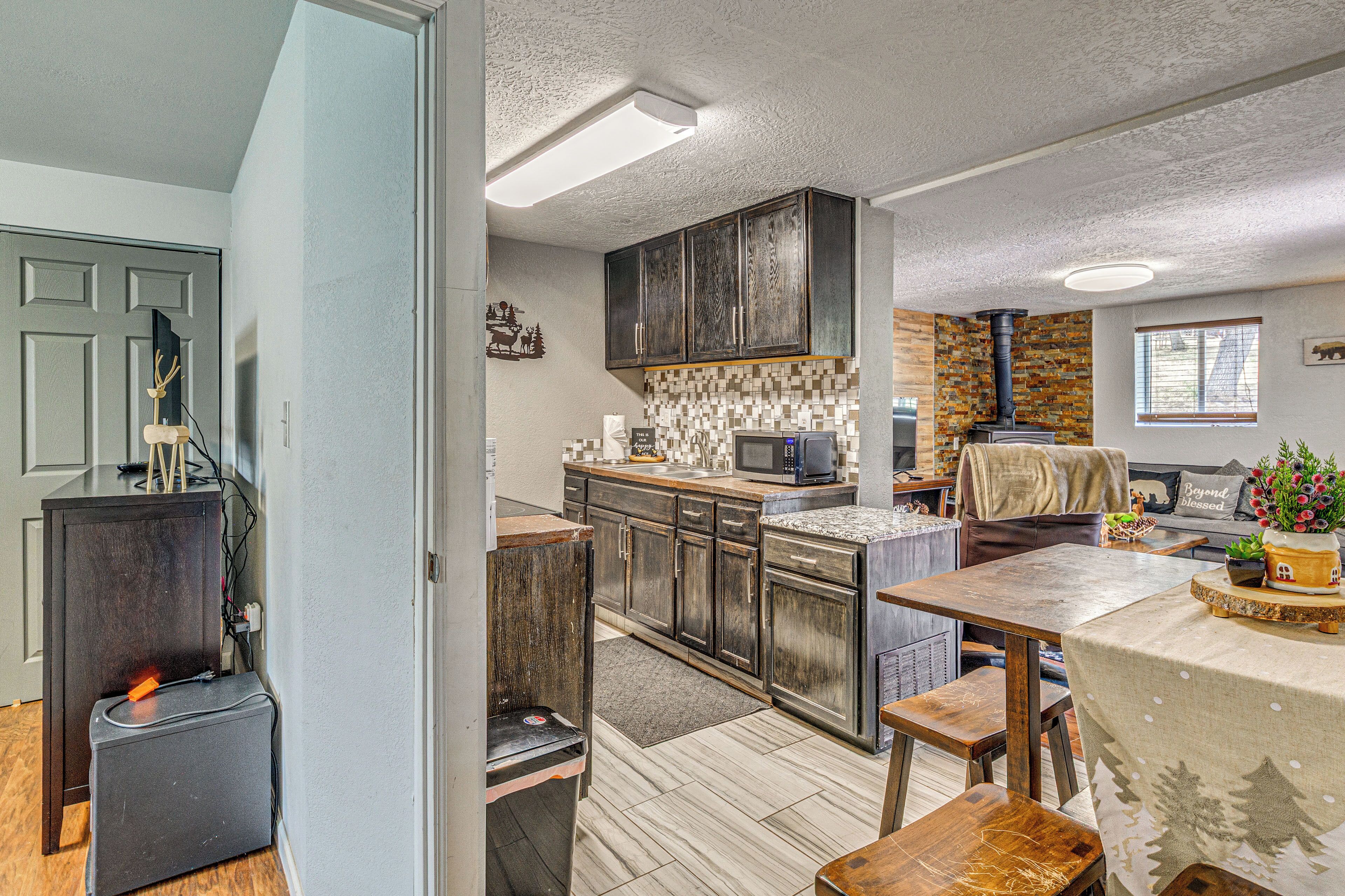 A kitchen with dark wooden cabinets, a tiled backsplash, a built-in microwave, and a large island with a tablecloth.