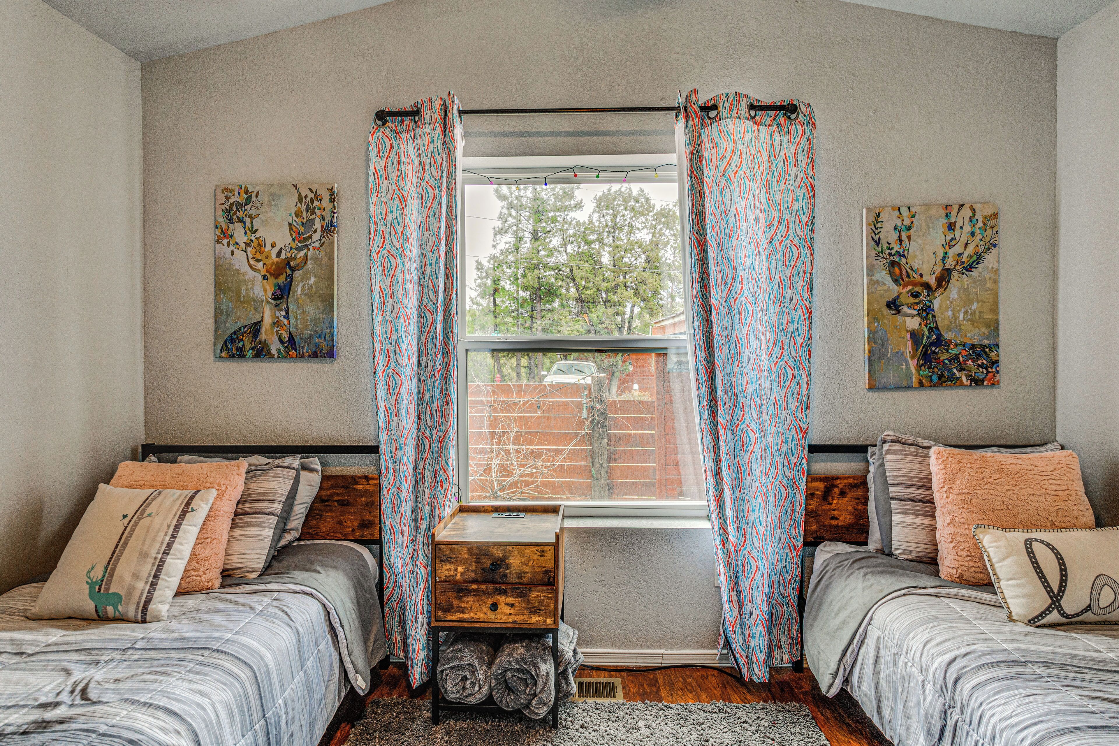 A bedroom with two beds, a window with curtains, and two wall-mounted paintings.