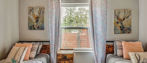 A bedroom with two beds, a window with curtains, and two wall-mounted paintings.