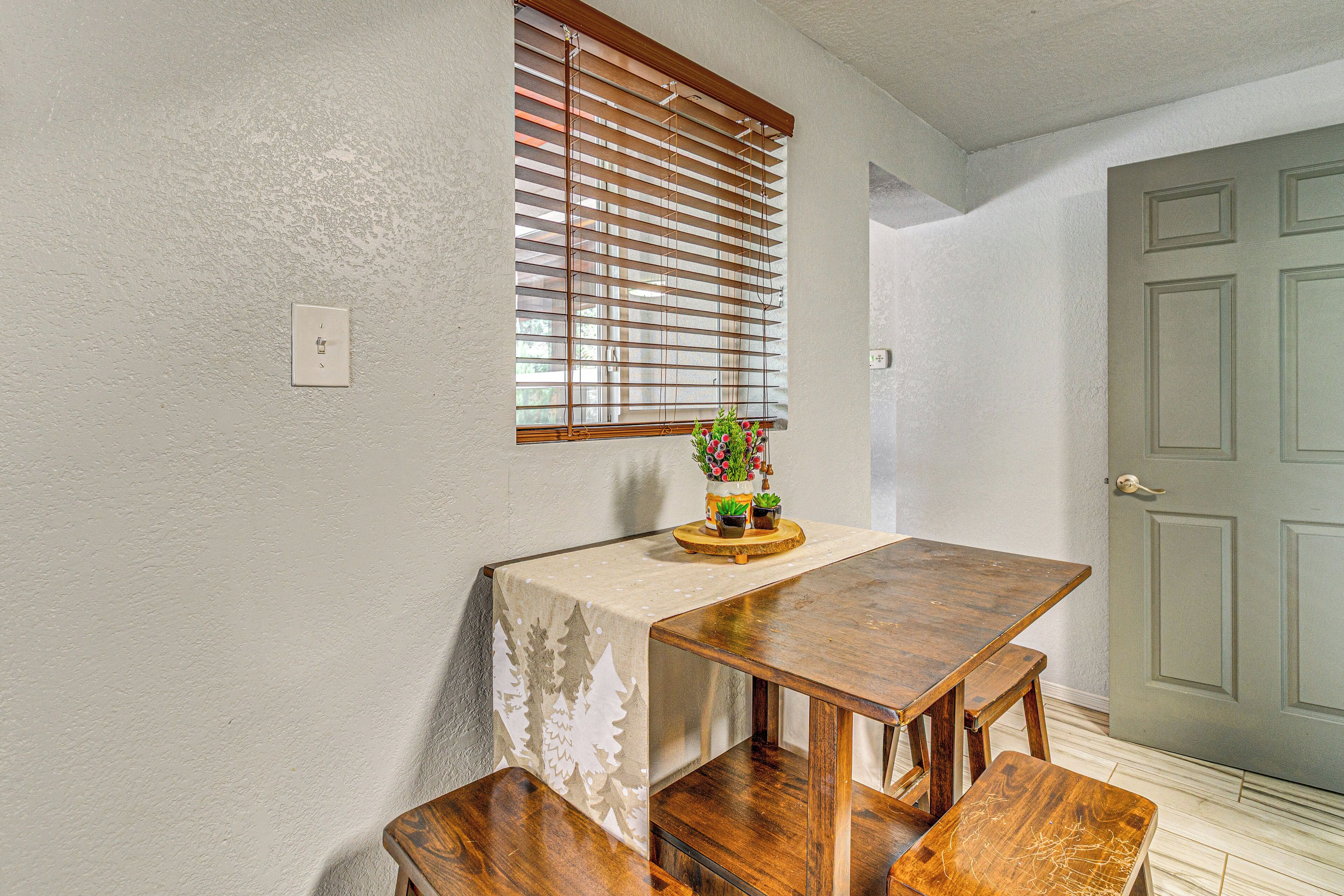 Un comedor con una mesa de madera y bancos, una ventana con persianas y una puerta con manija.