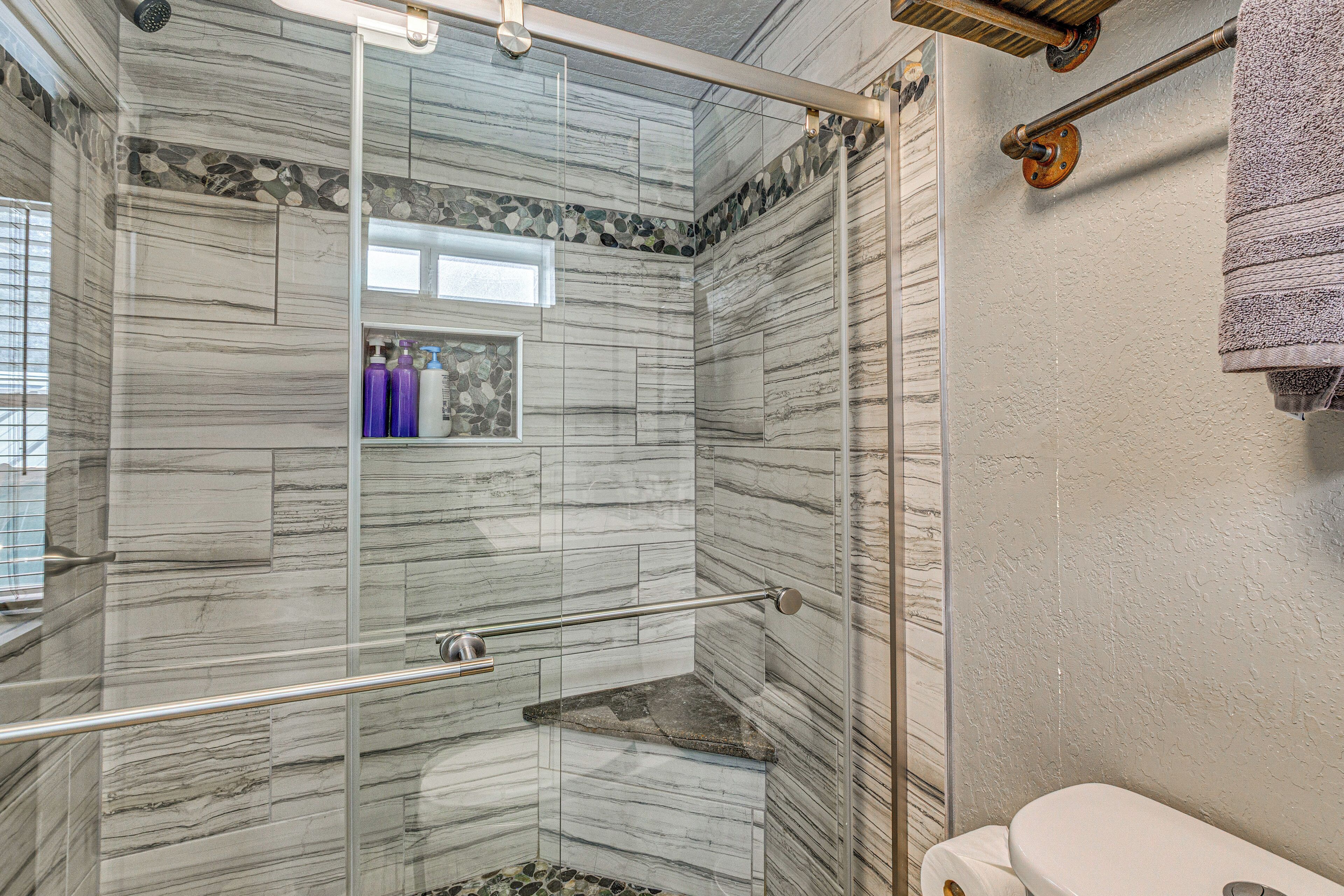 A bathroom with a glass shower enclosure, a marble wall, and a toilet.