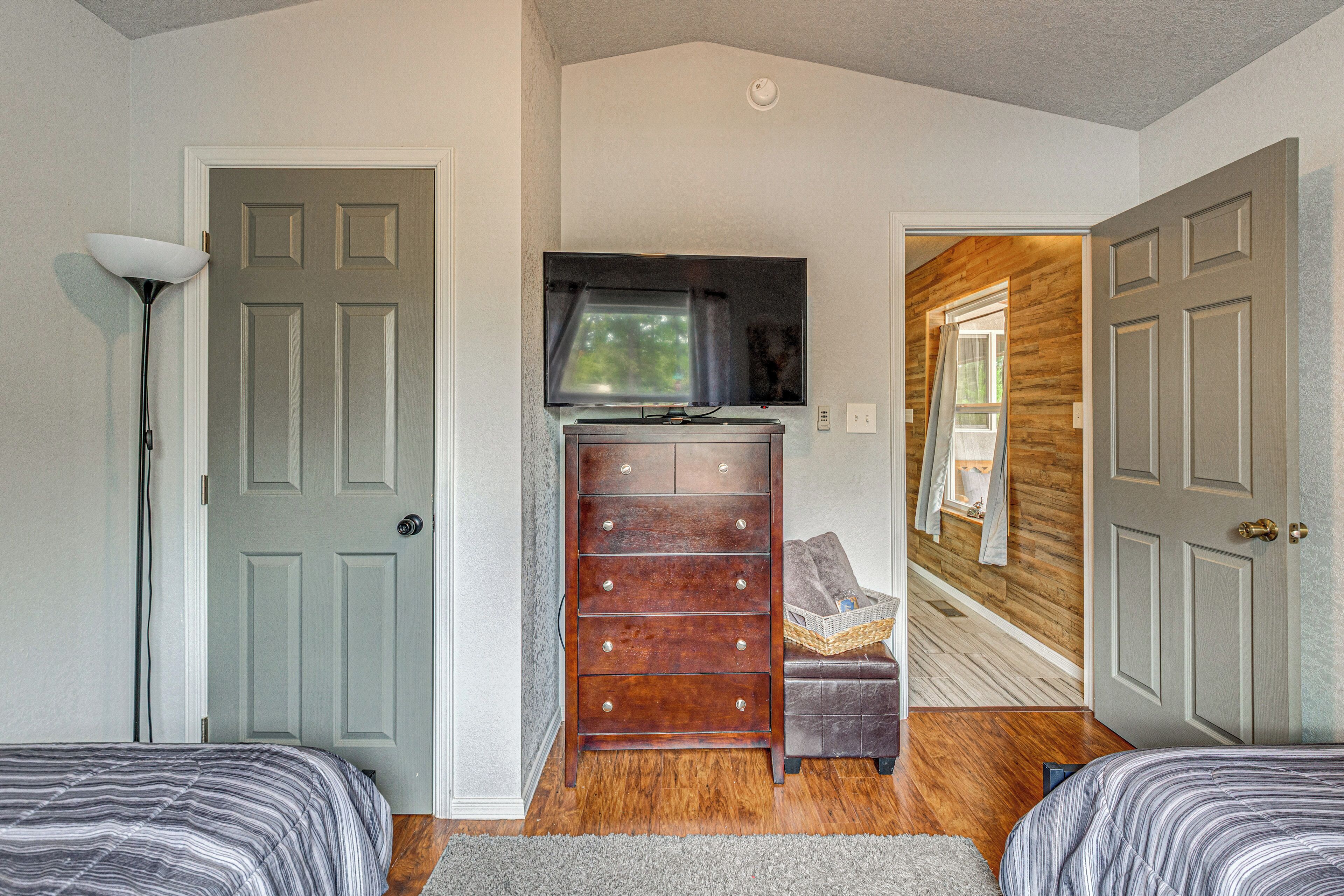 A bedroom with two beds, a dresser, a television, and a hallway leading to another room.