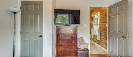 A bedroom with two beds, a dresser, a television, and a hallway leading to another room.