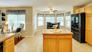 A kitchen with wooden cabinets, a black refrigerator, and a dining area with a table and chairs. - Pets Welcome: Convenient Family Home in Westland! (Westland)