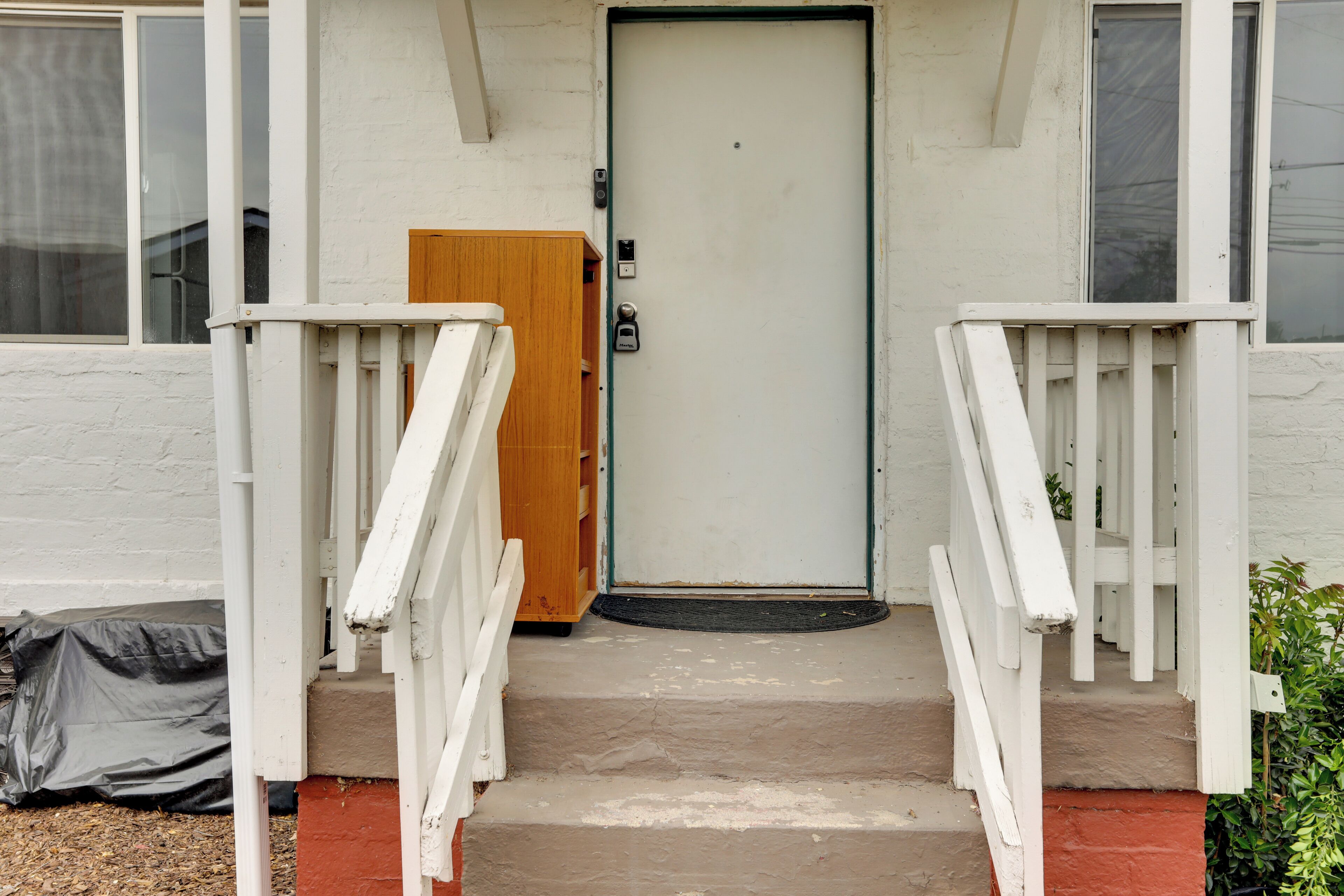 A white building with a wooden door, a set of white stairs, and a small porch area.