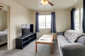 A living room with a sofa, a TV on a stand, a coffee table, and a ceiling fan. - Home Near Reno Industrial Center & Med Centers (Sparks)