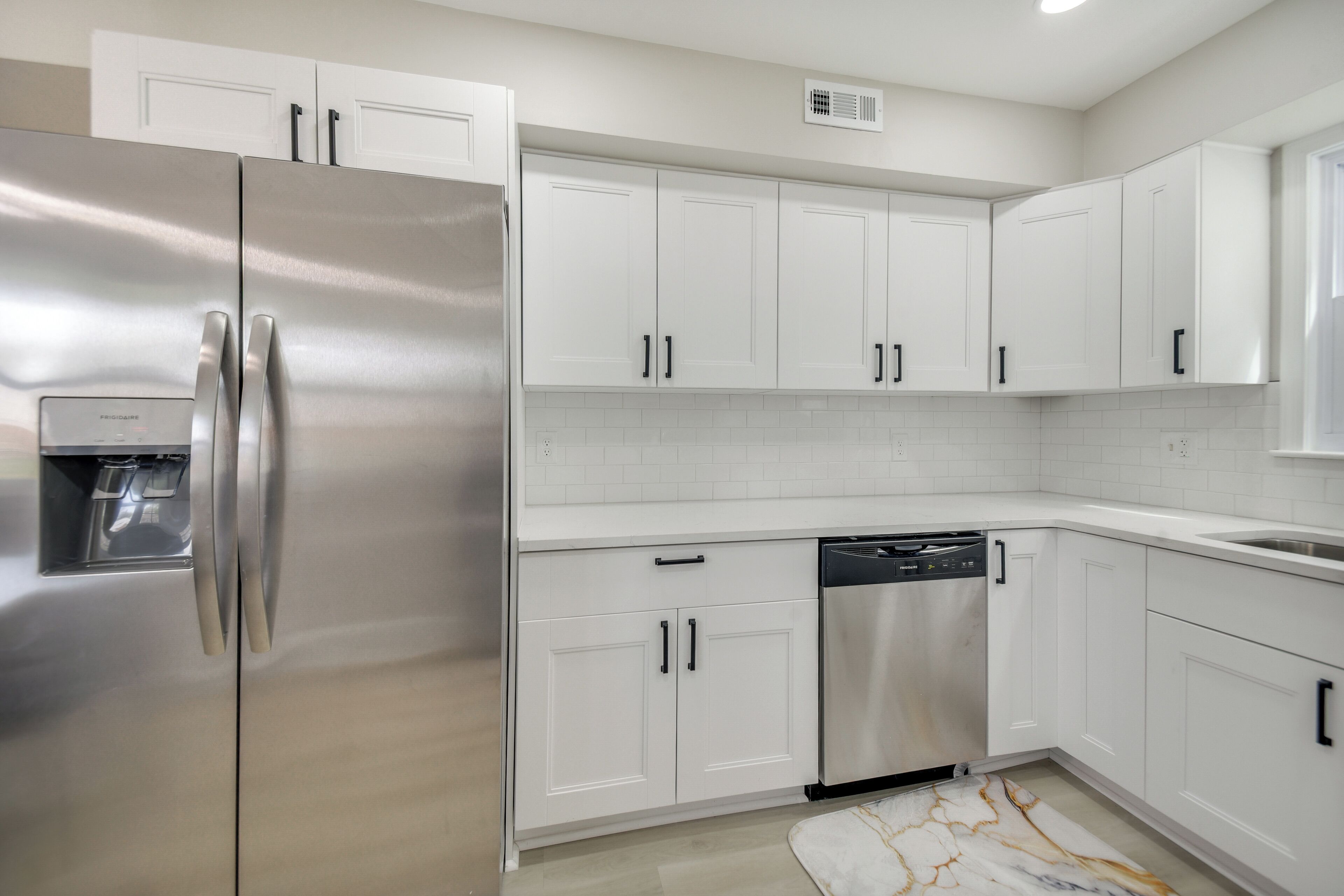 Una cocina moderna con armarios blancos, electrodomésticos de acero inoxidable y una alfombra con diseño de mármol.