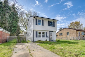 A two-story residential building with a front yard, a paved driveway, and a chain-link fence.