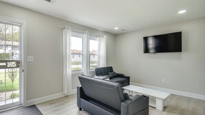 A modern living room with a sofa, a bench, a flat-screen TV, and a door with a view of the outside. - Near Waterfront! Retreat 6 Mi to Hampton Coliseum (Newport News)