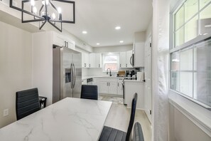 A modern kitchen with white cabinets, a marble countertop, and a dining area with a table and chairs. - Near Waterfront! Retreat 6 Mi to Hampton Coliseum (Newport News)