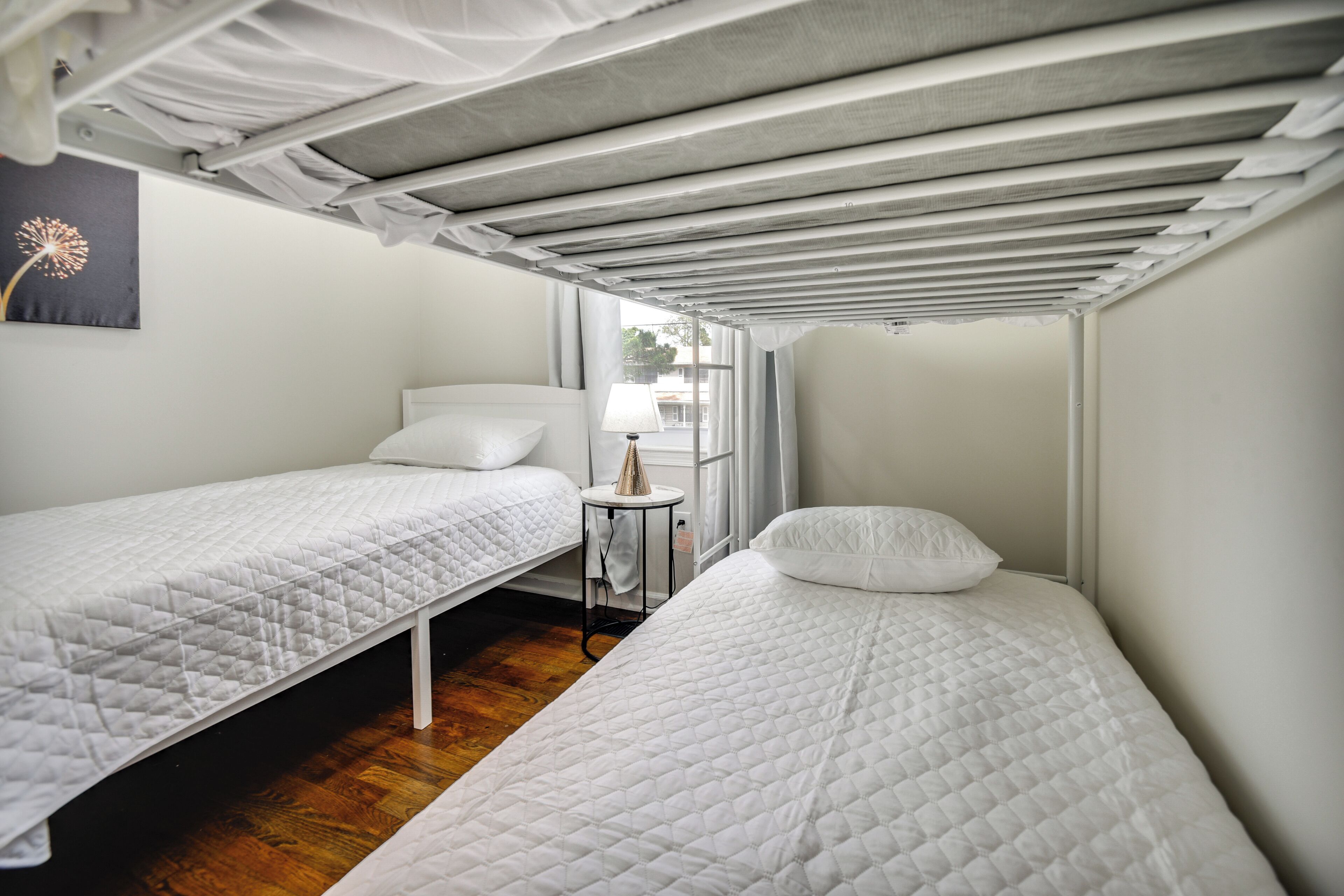 A small, compact room with two single beds, a small table, and a window providing natural light.