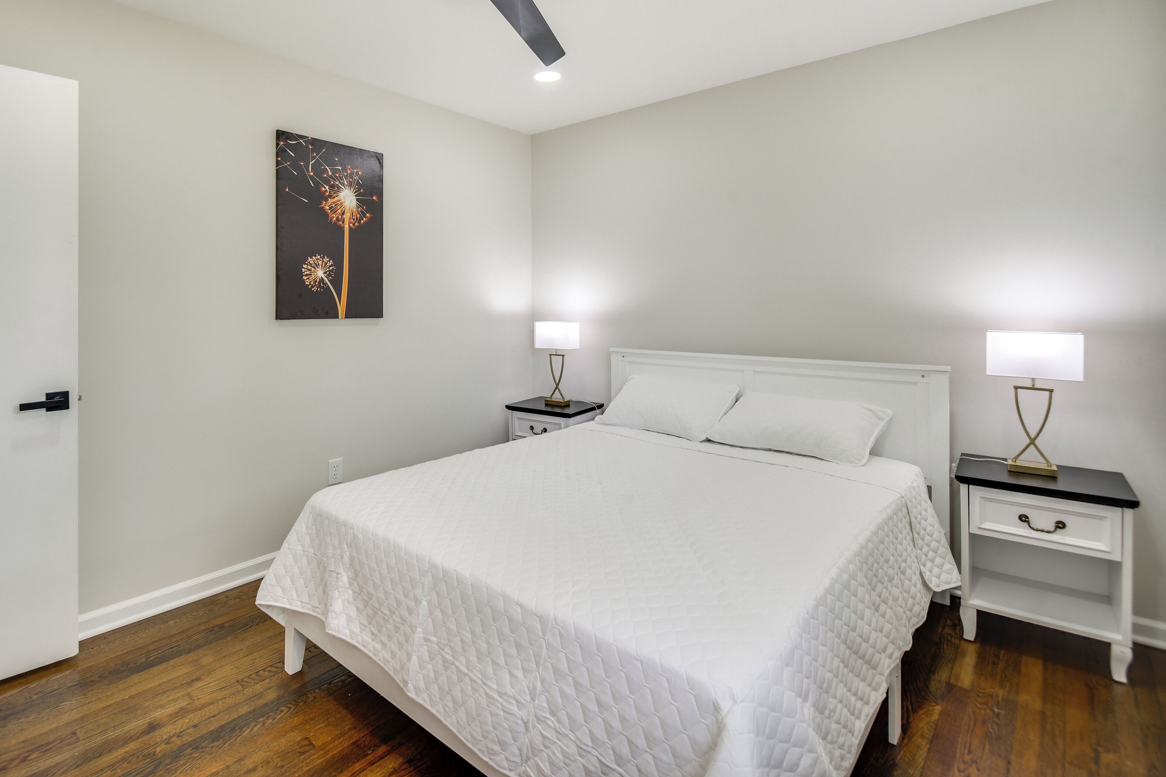 Un dormitorio con cama, mesitas de noche, una lámpara de pared y una puerta.