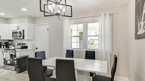 A modern kitchen with white cabinets, a stainless steel refrigerator, and a dining area with a white table and black chairs. - Near Waterfront! Retreat 6 Mi to Hampton Coliseum (Newport News)