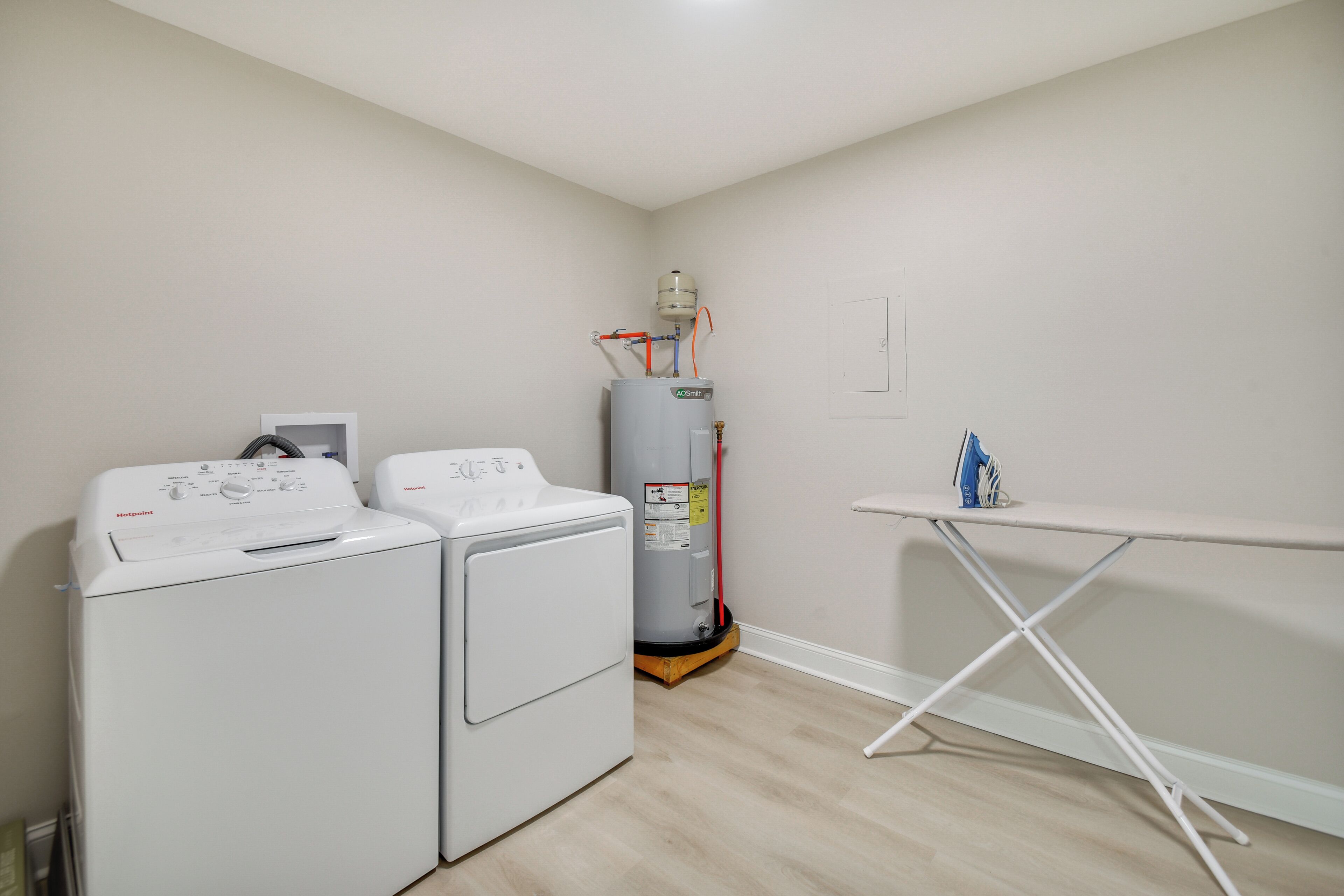 A laundry room with two front-loading washers, a water heater, and a table with ironing equipment.