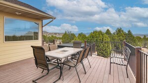 Um terraço com mesa, cadeiras, um banco e vista para árvores e montanhas.