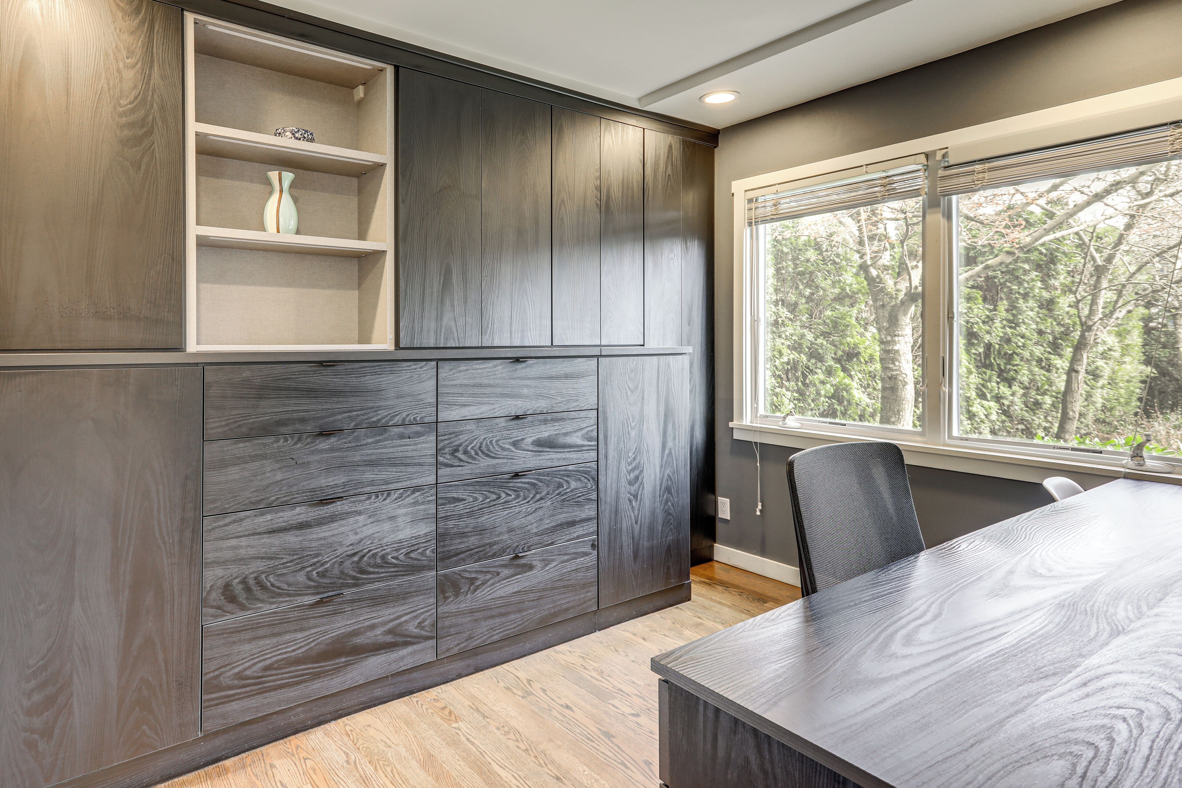 A modern kitchen with built-in cabinets, a dining table, and a window with a view of trees.