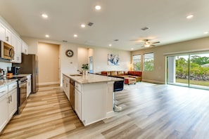 A spacious kitchen with a central island, a dining area with a sofa, and large windows offering a view of the outdoors. - Home < 1-mi Walk to Warm Mineral Springs Park! (North Port)