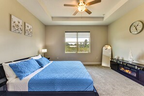 A bedroom with a bed, a ceiling fan, a fireplace, a clock, and a window with blinds.