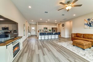 Una cocina moderna con una isla central, un comedor con taburetes de bar, una chimenea y una sala de estar con sofá y reposapiés.