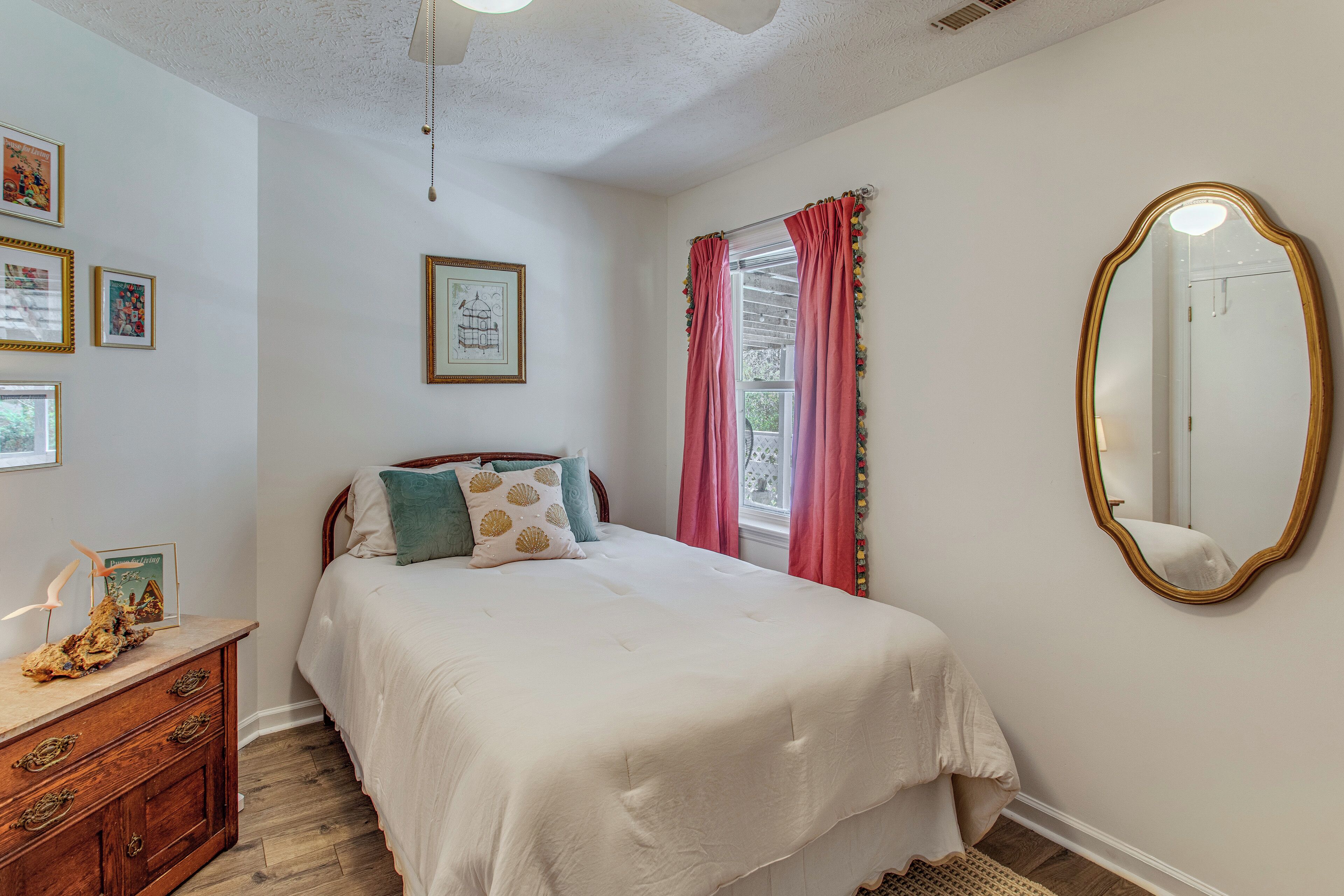 A bedroom with a bed, dresser, mirror, and wall art.