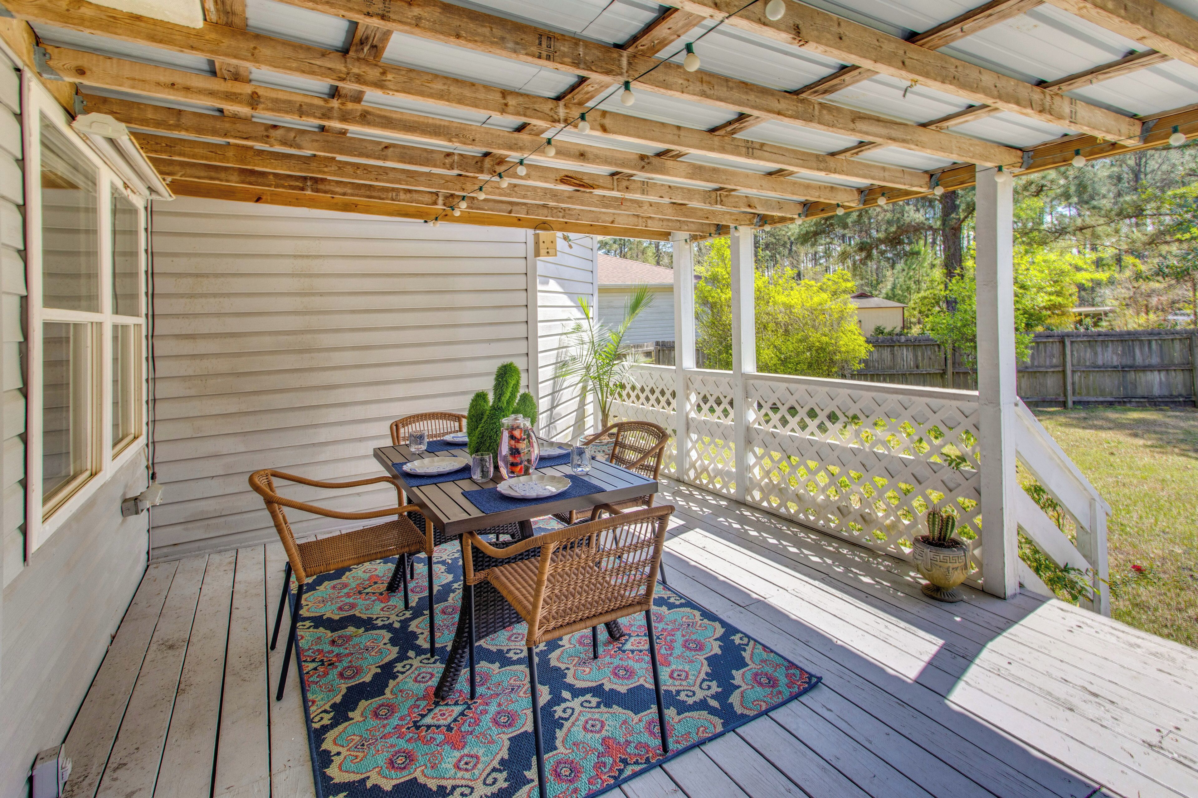 A covered patio with a table set for dining, surrounded by wicker chairs and a patterned rug.
