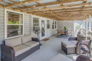 A covered porch with wicker furniture, a fan, and string lights.