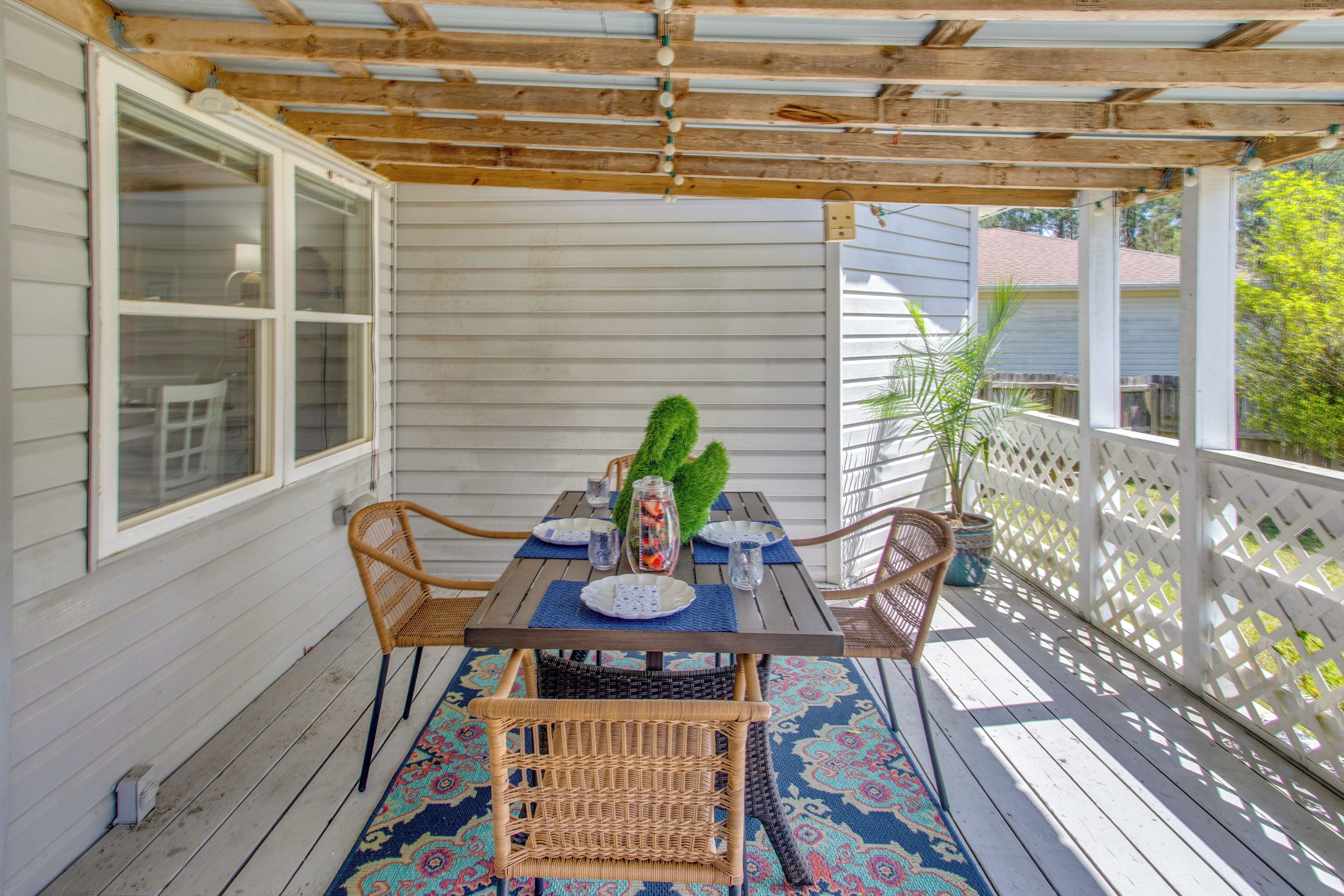 Une terrasse couverte avec une table dressée pour deux personnes, entourée de chaises en osier, d’un tapis à motifs et d’une plante en pot.