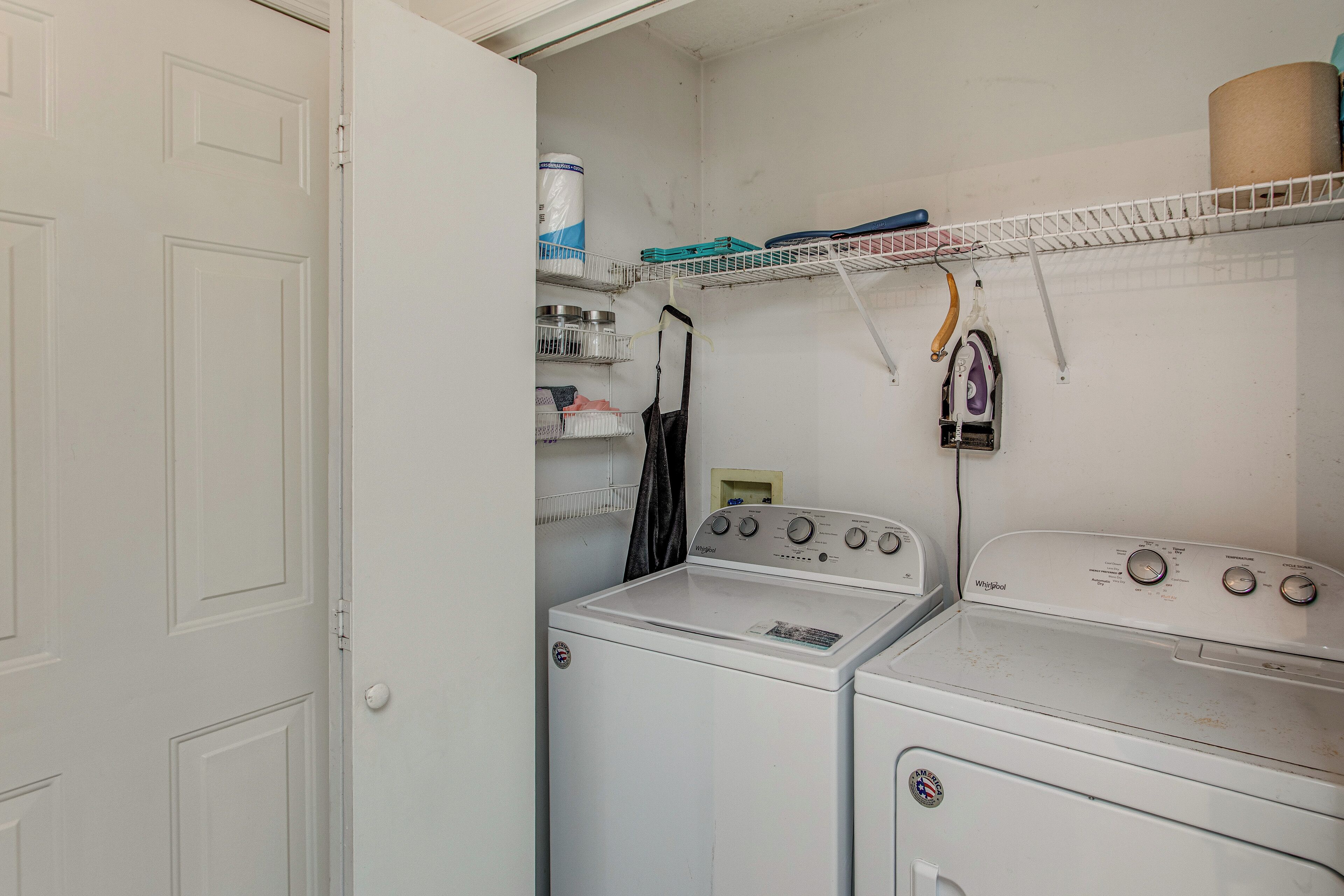 A laundry room with a washer and dryer, shelves with laundry supplies, and a door.