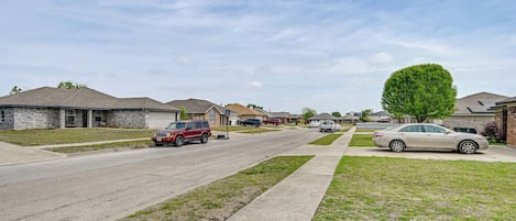 A residential street with houses, a sidewalk, and parked cars.