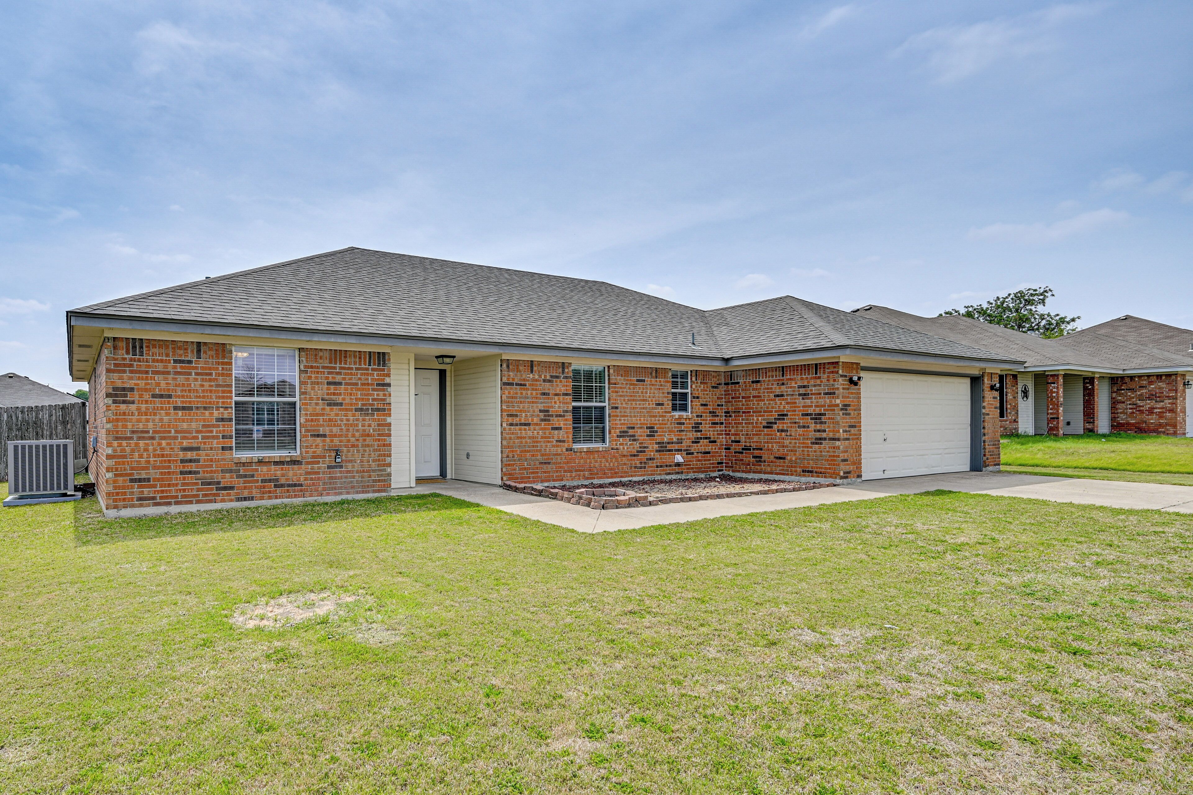 A single-story brick house with a garage, a front lawn, and a clear sky.