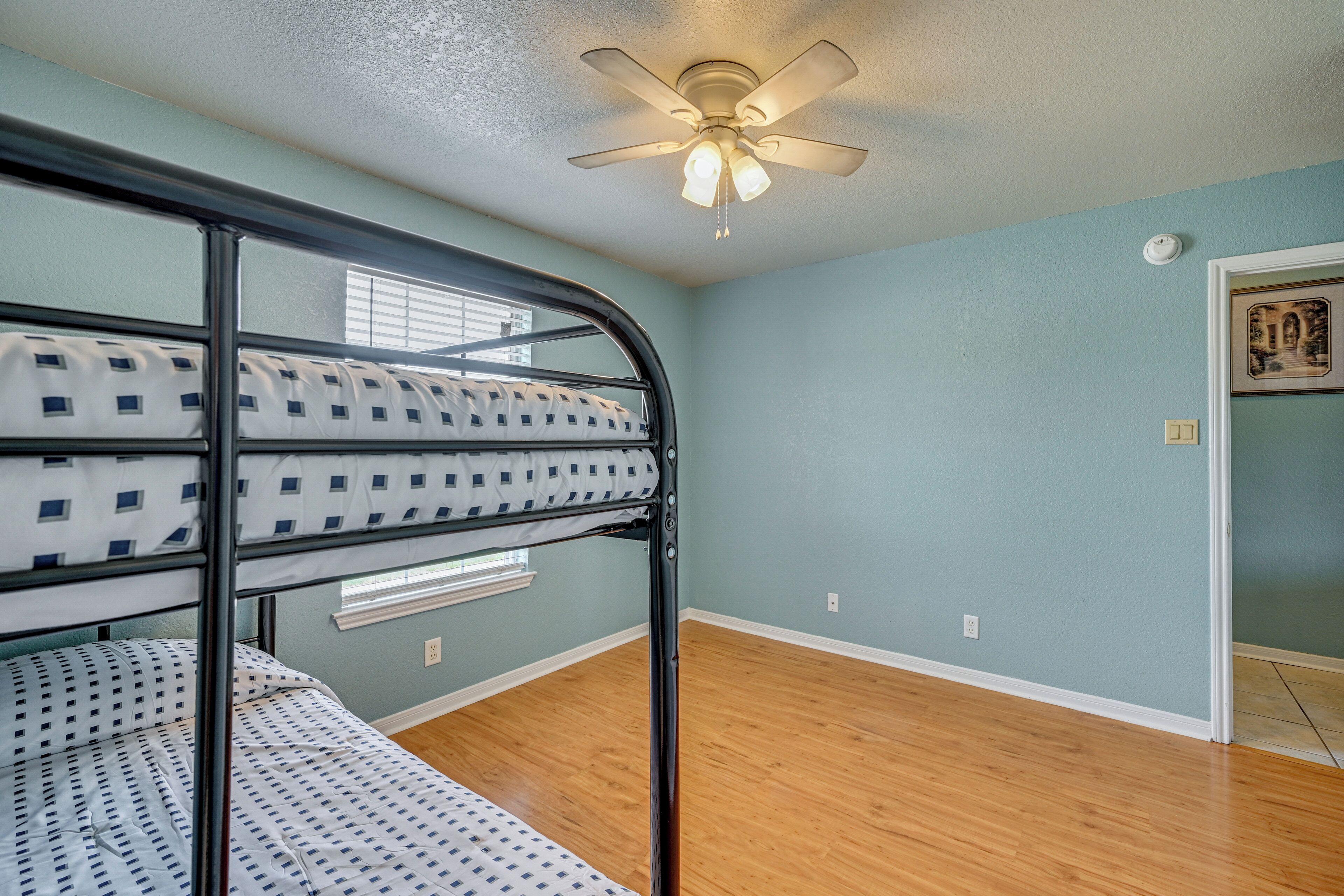 A room with bunk beds, a ceiling fan, and a door leading to another room.