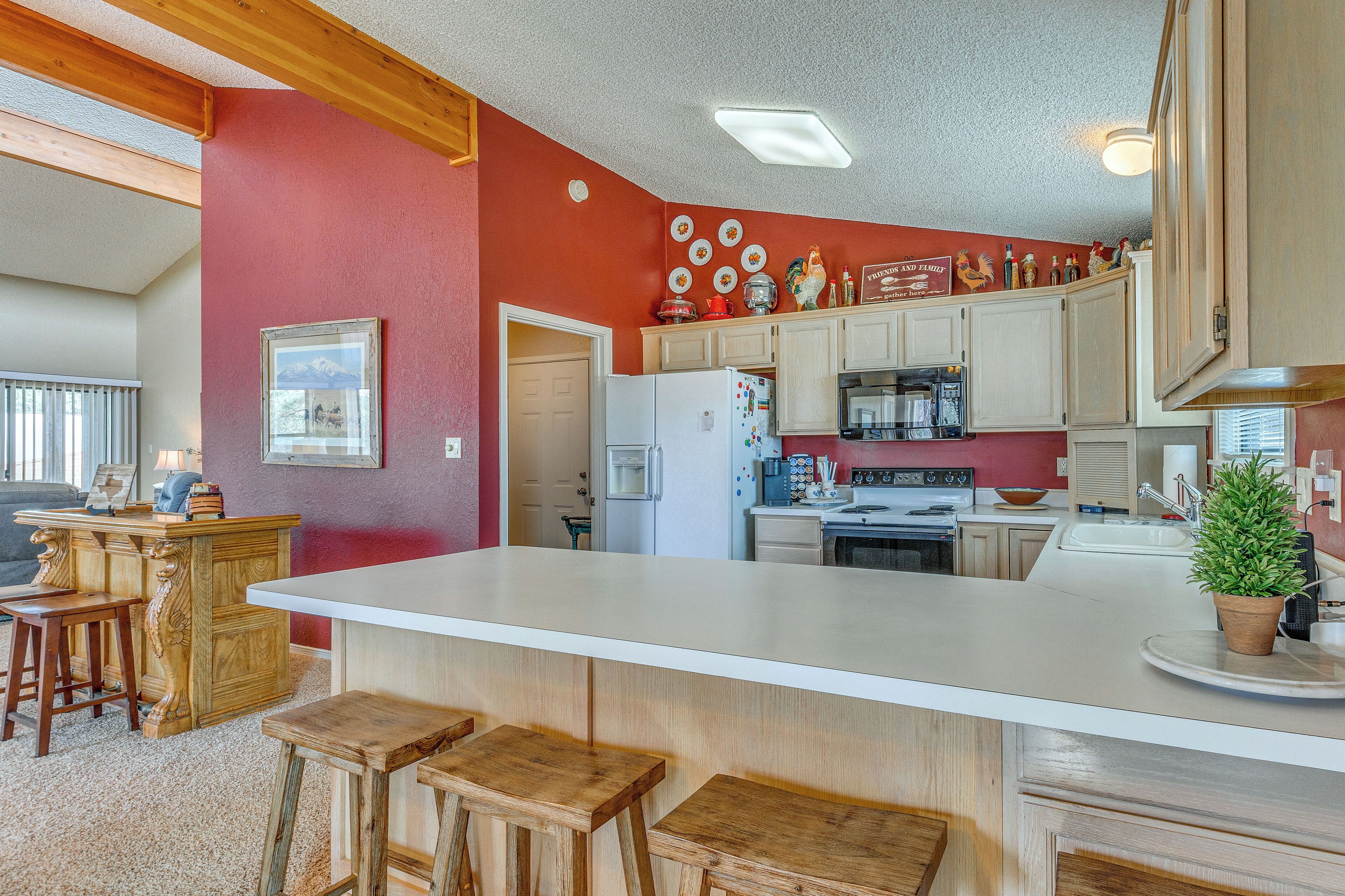 A kitchen with a large island, wooden stools, and a red accent wall.