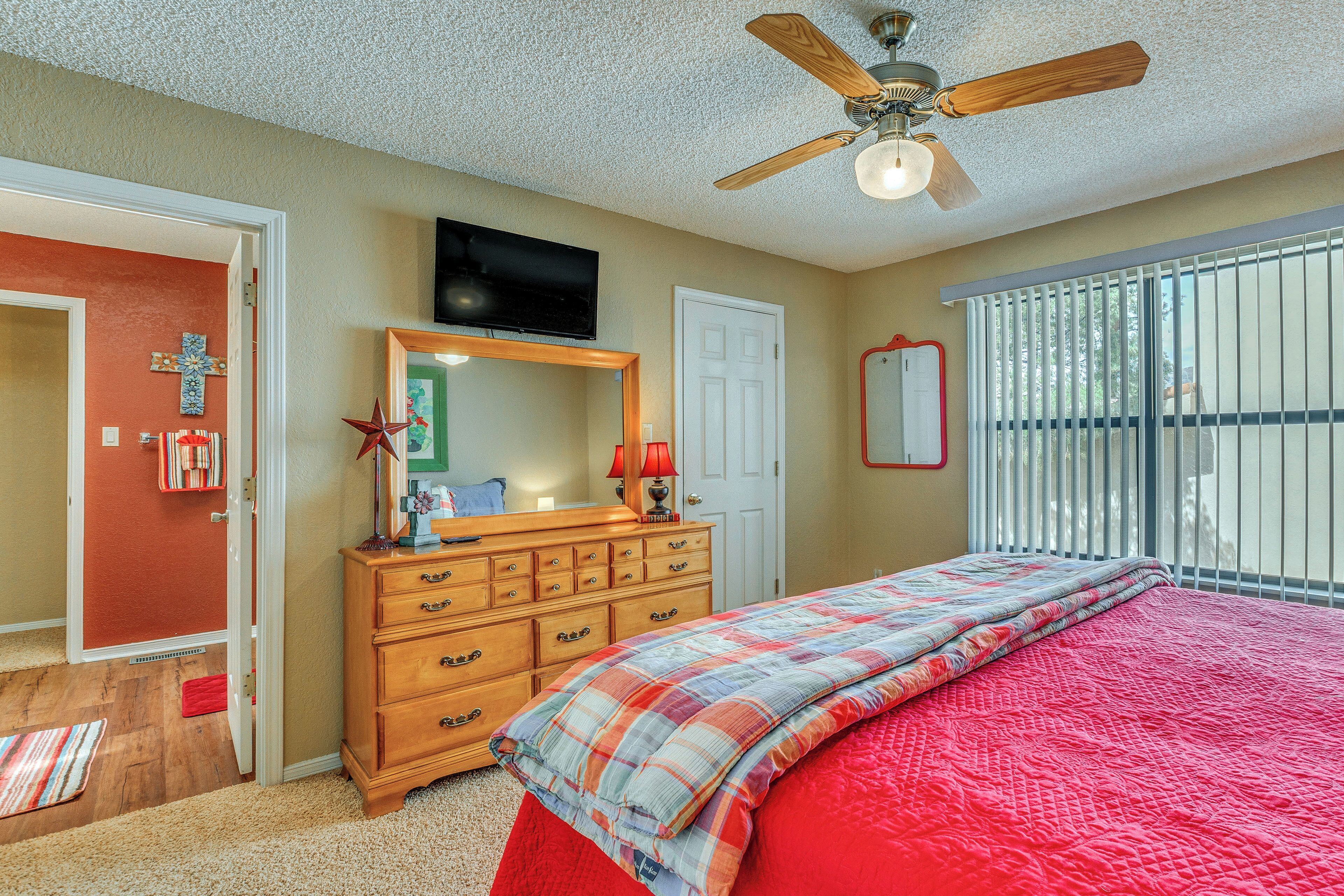 A bedroom with a bed, dresser, ceiling fan, TV, and a window with blinds.