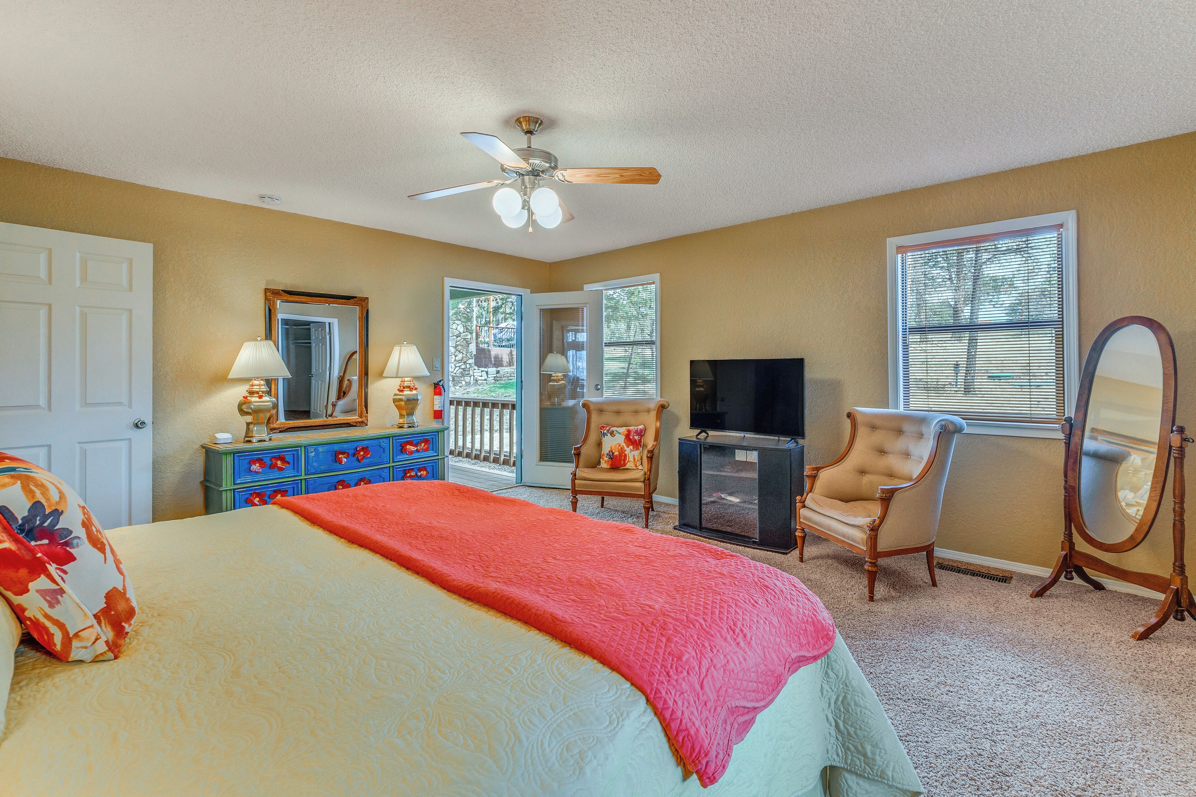 A bedroom with a bed, dresser, TV, chairs, and a ceiling fan.