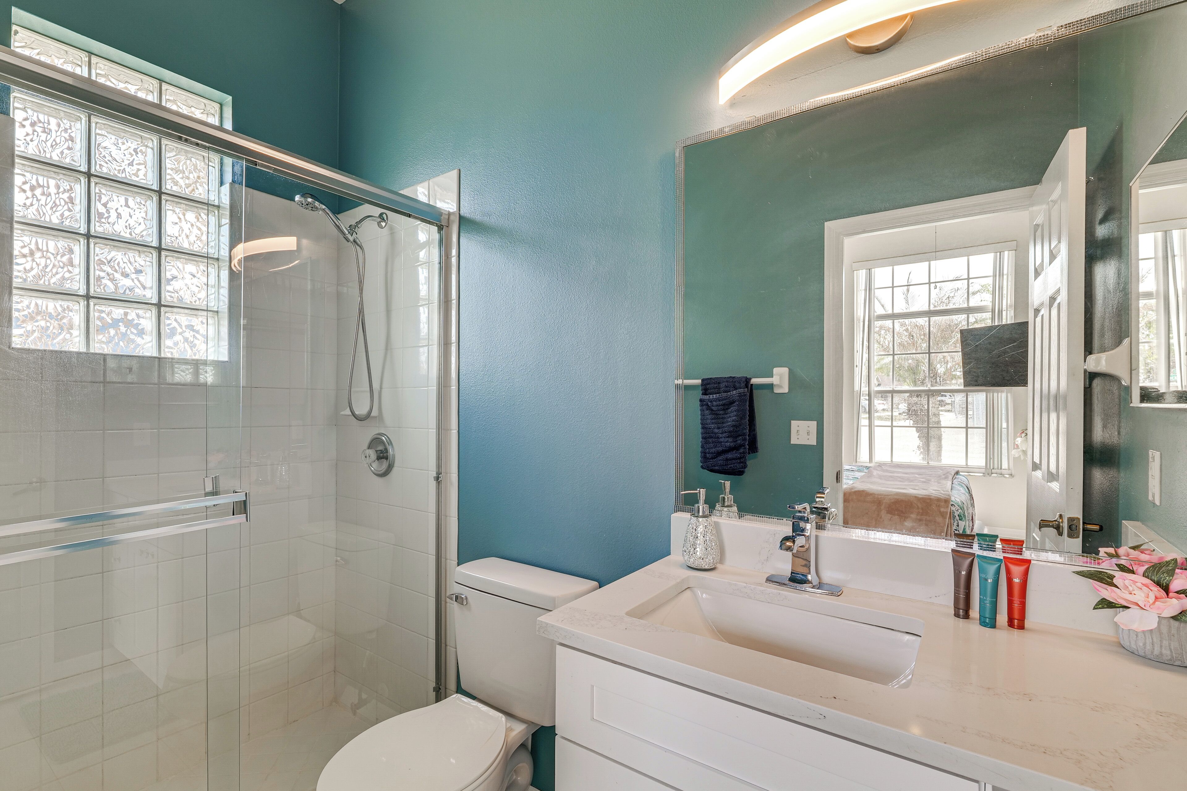 A bathroom with a glass shower enclosure, a toilet, a sink with toiletries, and a mirror.
