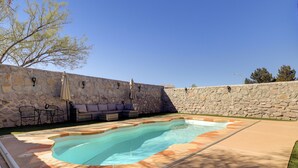 Piscina com paredes de pedra, área de pátio e mobiliário para exterior.