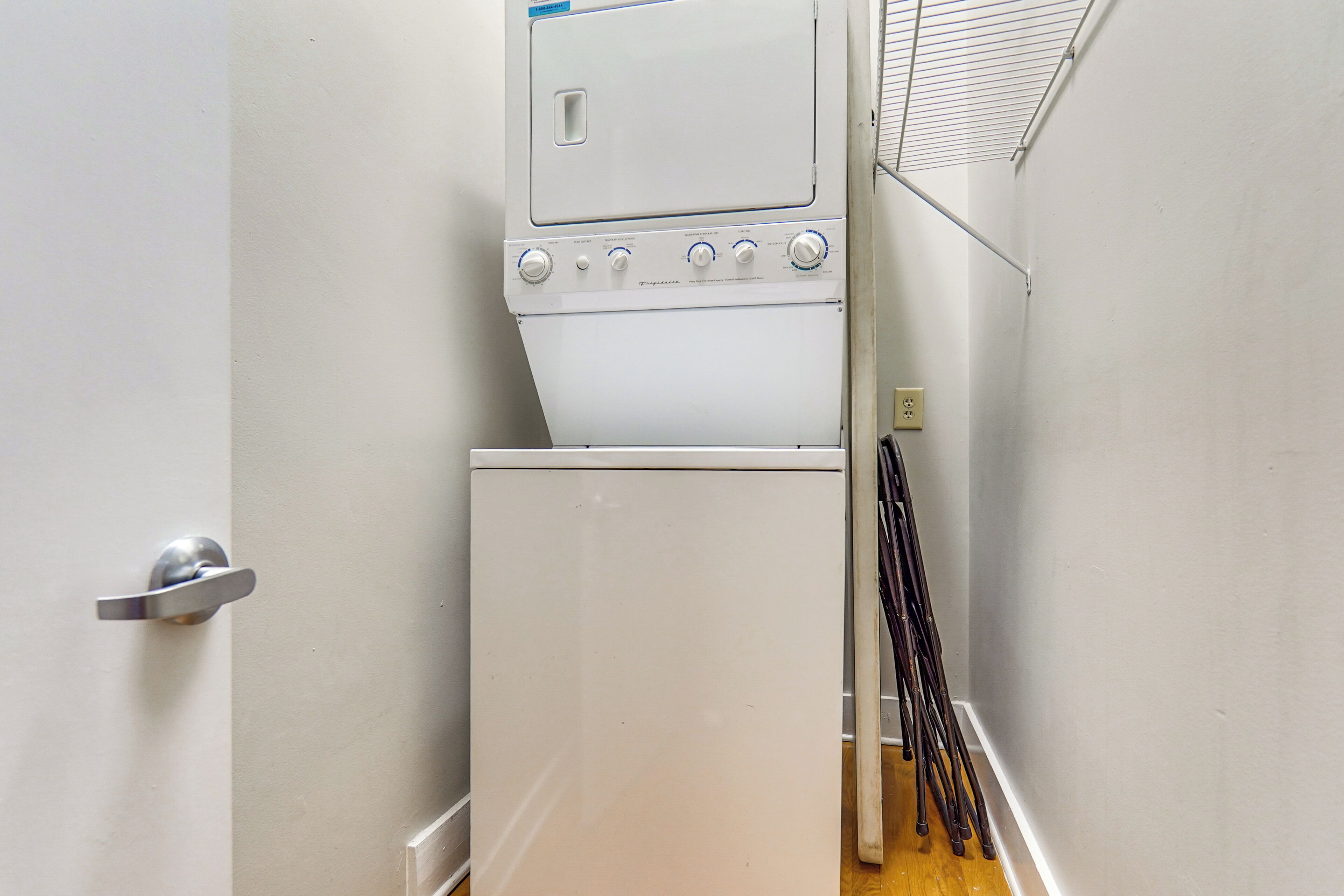 Une buanderie équipée d’un lave-linge et d’un sèche-linge, une porte avec une poignée argentée et un étagère en métal sur laquelle sont posés divers objets.