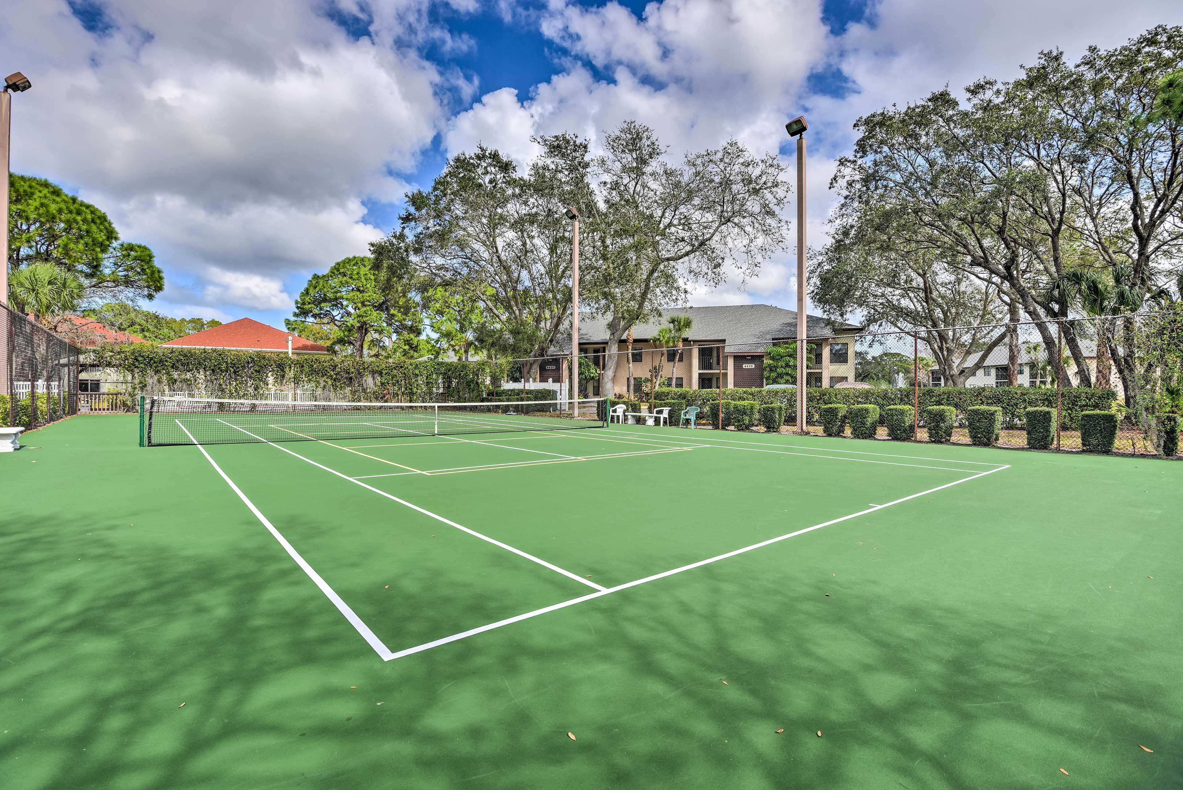 Una cancha de tenis con red, rodeada de árboles y edificios.