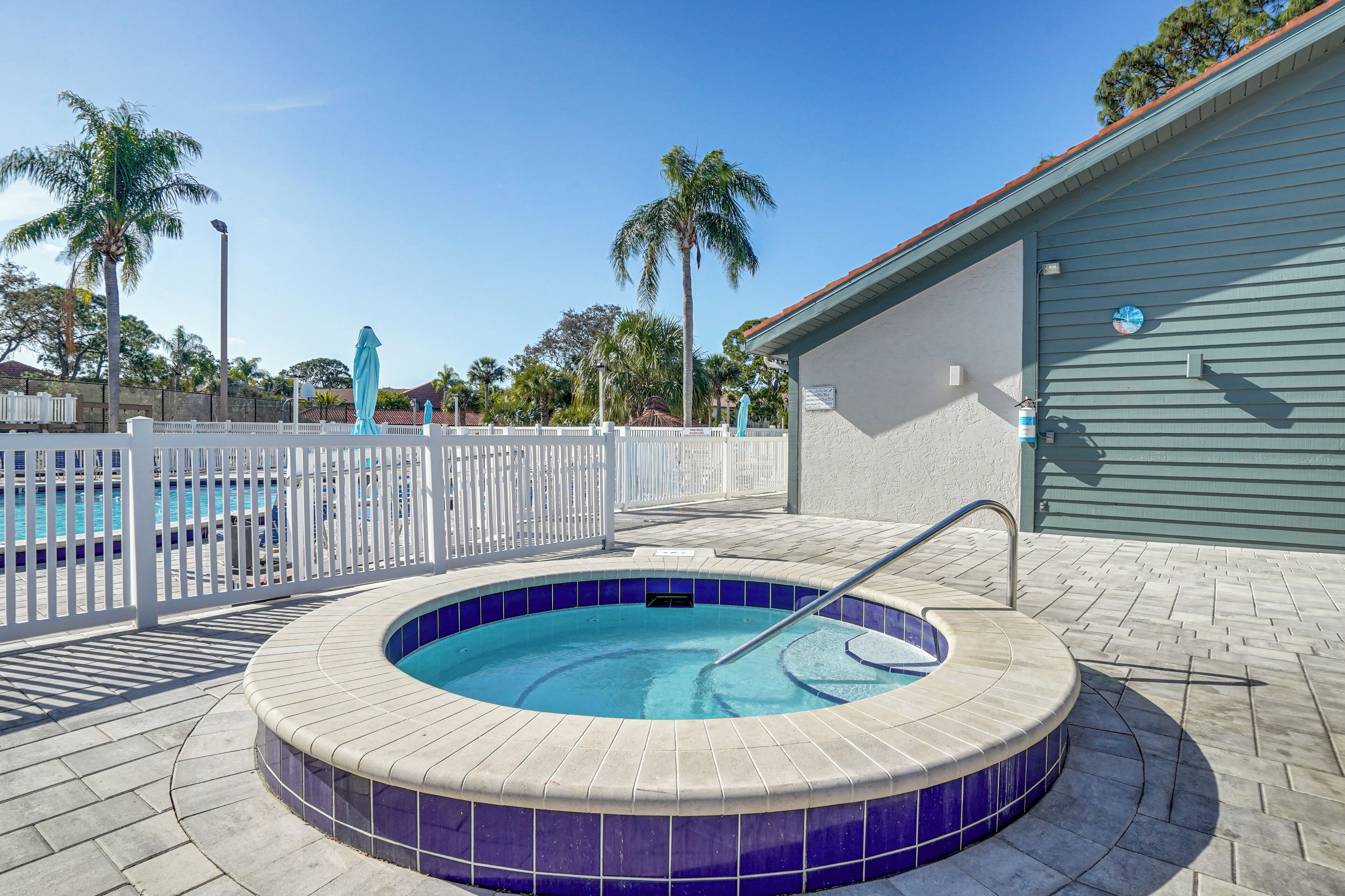 Une piscine avec un jacuzzi, entourée d’une clôture blanche, de palmiers et d’un bâtiment à la façade bleue.