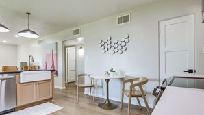 Eine moderne Küche mit Holzschränken, einer weißen Arbeitsplatte, einem runden Tisch mit Stühlen und einer Wandplatte als Dekoration.
