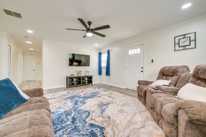 A living room with a ceiling fan, a large rug, two couches, a TV, and a clock on the wall.