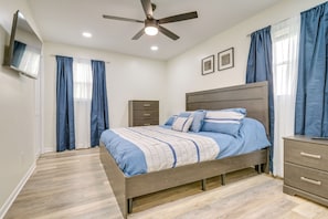 A bedroom with a bed, a nightstand, a dresser, a ceiling fan, and two wall-mounted picture frames.
