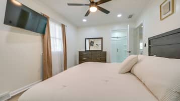 Un dormitorio con una cama, ventilador de techo, televisor, cómoda y una puerta que da a un baño.