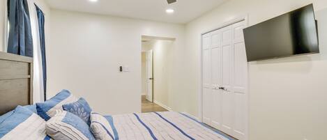A bedroom with a bed, ceiling fan, TV, wardrobe, and a hallway leading to another room.