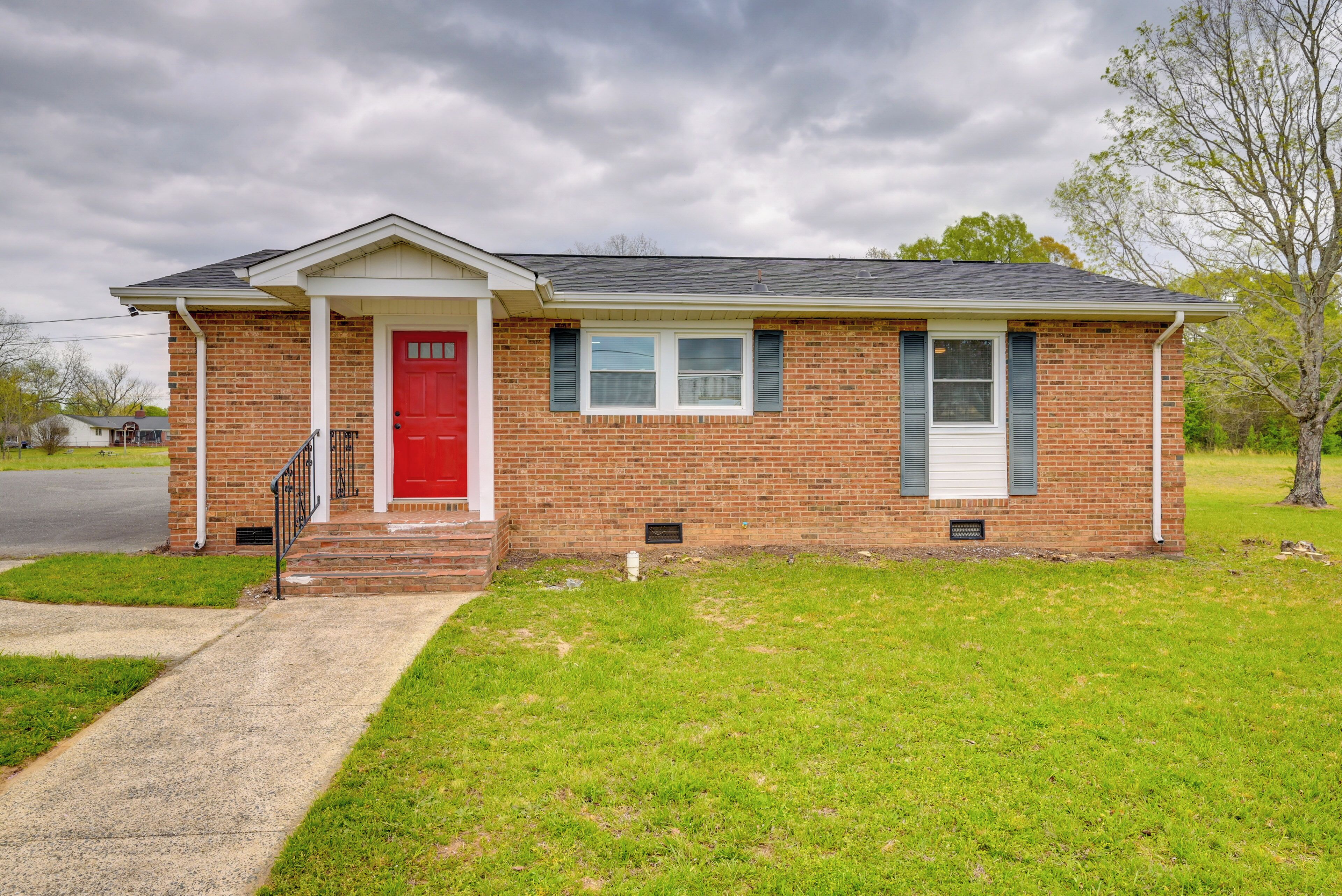 A single-story brick house with a red front door, white trim, and a small front porch.