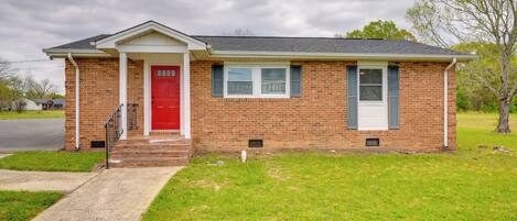 A single-story brick house with a red front door, white trim, and a small front porch.