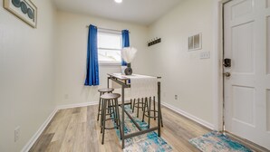 Une pièce comprenant une table et des tabourets, une fenêtre avec des rideaux, une porte et un luminaire fixé au mur.