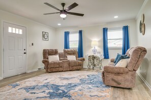 A living room with two recliner sofas, a ceiling fan, a patterned rug, and a window with blue curtains.