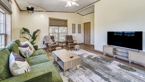 Un salon avec un canapé vert, une table basse, un téléviseur et un ventilateur de plafond.